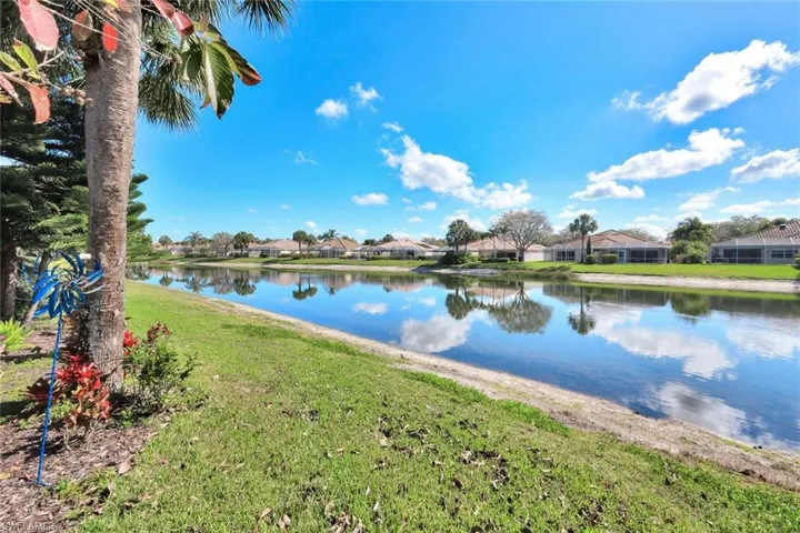 Waterfront property featuring a tranquil lake, lush green lawn, mature palm trees, and residential structures with tiled roofs