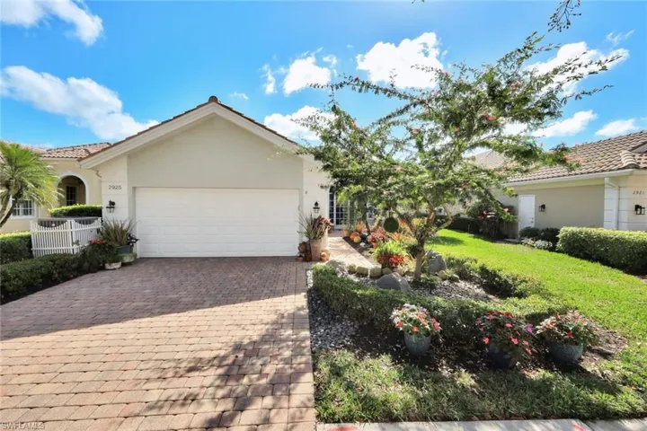 Stucco exterior residence with a tiled roof, paver driveway, and an attached garage