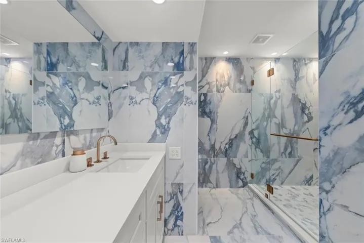 Full bath featuring stone wall, a marble finish shower, vanity, marble tiled flooring, and tile walls
