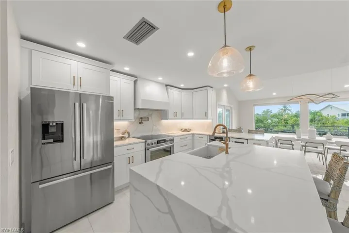 Kitchen featuring appliances with stainless steel finishes, white cabinetry, light stone countertops, vaulted ceiling, and a breakfast bar area