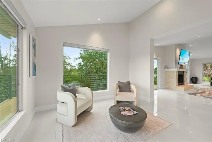 Sitting room featuring vaulted ceiling, plenty of natural light, a fireplace with raised hearth, tile patterned floors, and recessed lighting