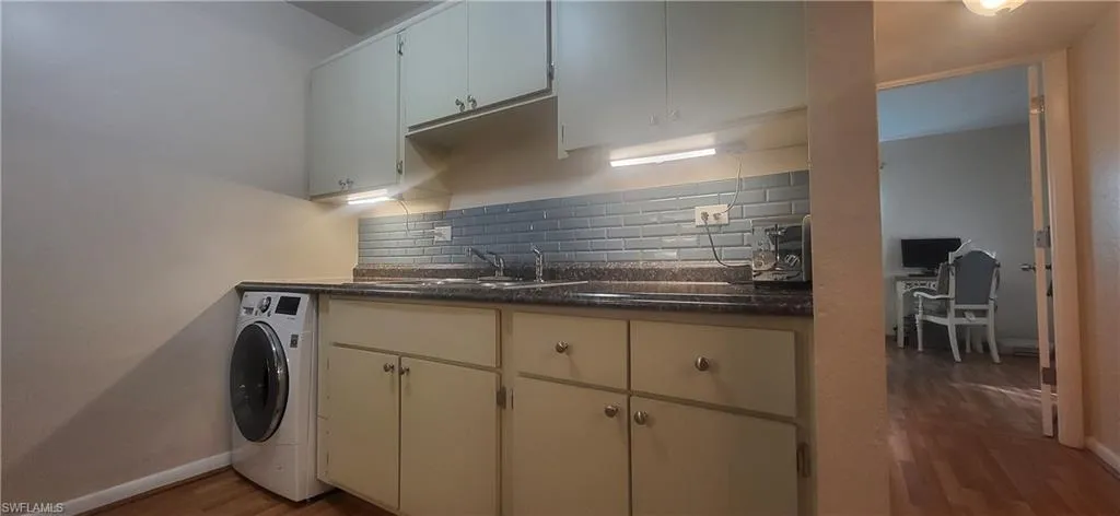 Kitchen featuring decorative backsplash, sink, white cabinets, washing machine and wood style floors
