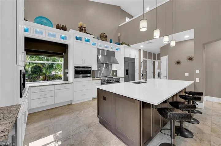 Kitchen with premium appliances, white cabinets, a center island with sink, and wall chimney exhaust hood