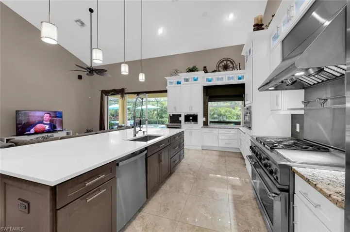 Kitchen with appliances with stainless steel finishes, wall chimney exhaust hood, sink, white cabinets, and a kitchen island with sink