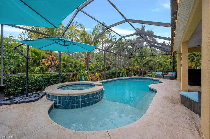 View of pool featuring glass enclosure, an in ground hot tub, a patio area, and an outdoor hangout area