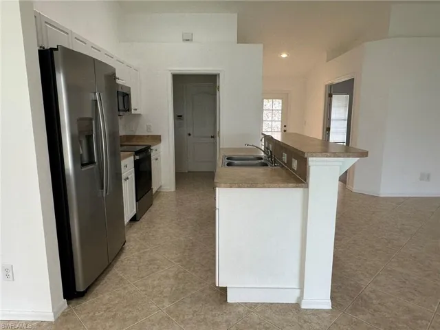 Kitchen with stainless steel appliances, white cabinets, light tile patterned flooring, recessed lighting, and a breakfast bar