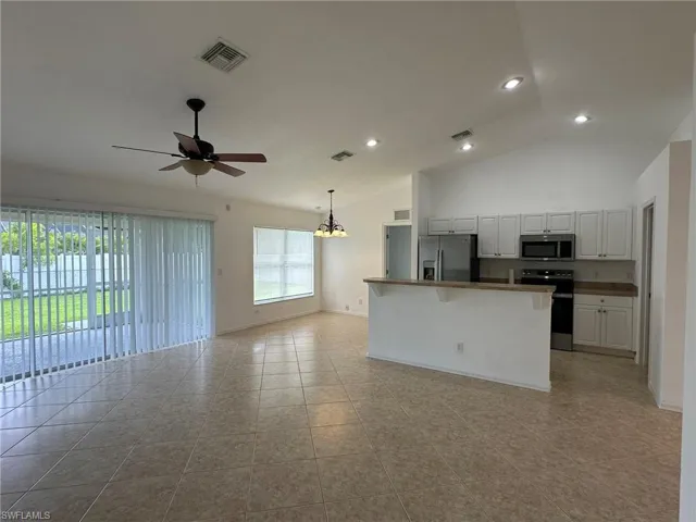 Kitchen with open floor plan, appliances with stainless steel finishes, a chandelier, a kitchen bar, and white cabinets