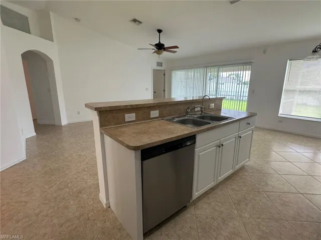 Kitchen featuring white cabinetry, a kitchen island with sink, stainless steel dishwasher, arched walkways, and light tile patterned flooring