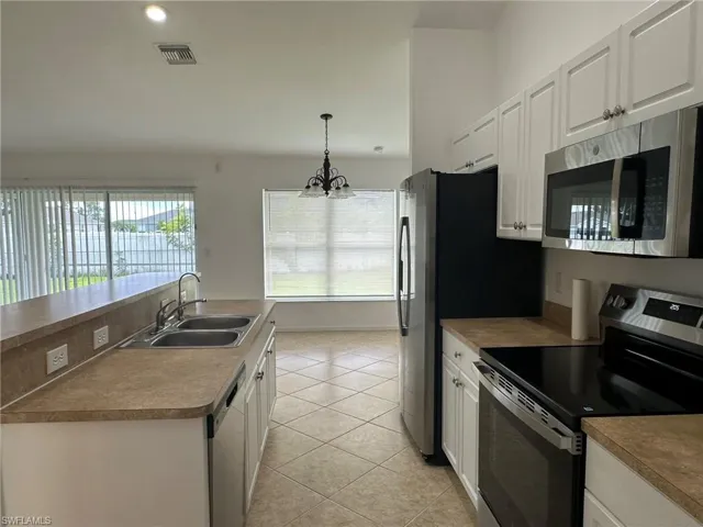Kitchen featuring stainless steel appliances, white cabinets, decorative light fixtures, light tile patterned flooring, and recessed lighting