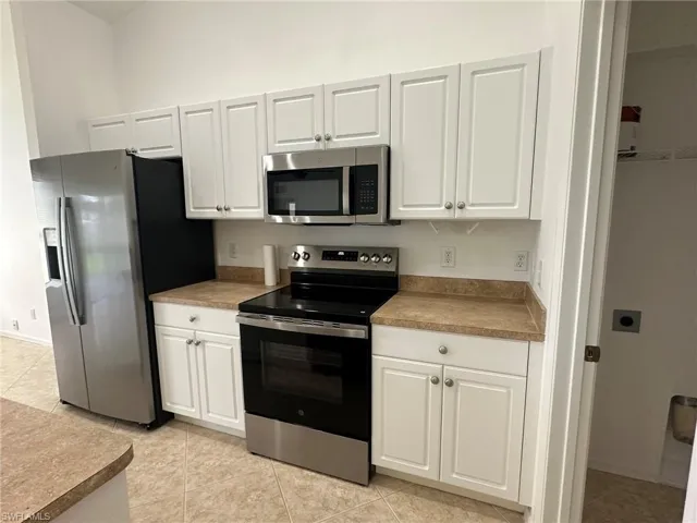 Kitchen with stainless steel appliances, light tile patterned flooring, and white cabinets