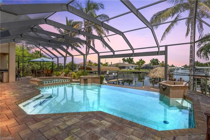 Pool at dusk with screened enclosure, an in ground hot tub, and a patio area