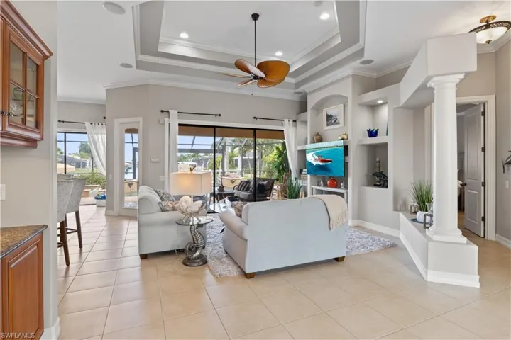 Tiled living room with ceiling fan, a wealth of natural light, ornate columns, and a raised ceiling
