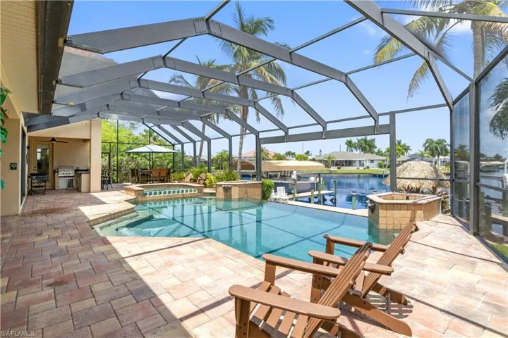 View of pool with screened enclosure, an in ground hot tub, and a patio with an outdoor kitchen