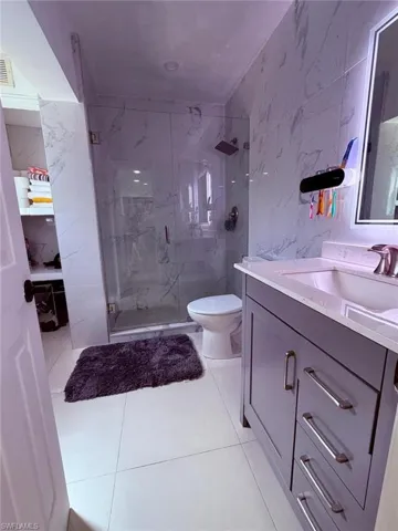 Full bath with vanity, a marble finish shower, tile walls, and stone wall