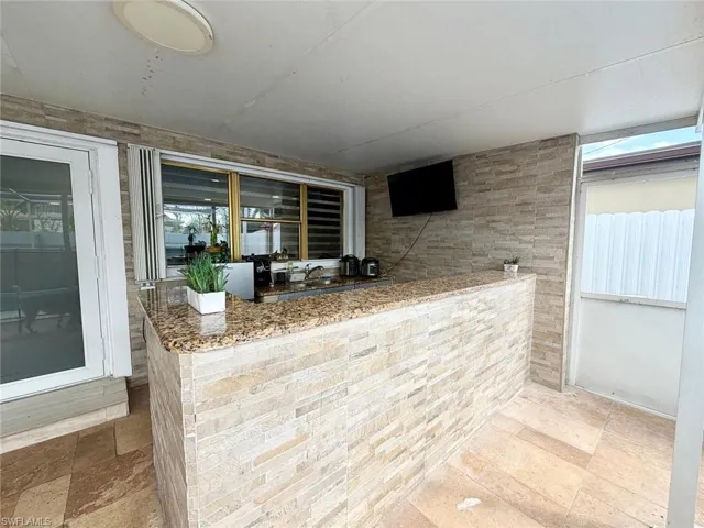Bar with light stone counters, healthy amount of natural light, and stone tile floors