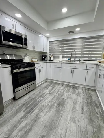 Kitchen featuring stainless steel appliances, white cabinetry, light wood-style floors, recessed lighting, and a raised ceiling