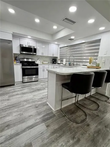 Kitchen with stainless steel appliances, white cabinets, a breakfast bar area, a peninsula, and recessed lighting