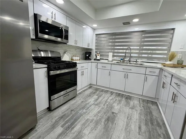 Kitchen with stainless steel appliances, light wood-style floors, recessed lighting, white cabinetry, and backsplash