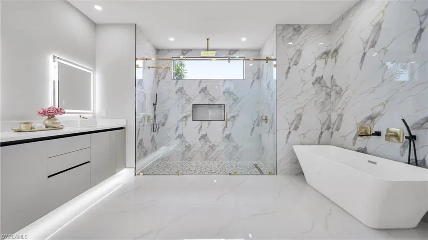 Full bath featuring vanity, a marble finish shower, a freestanding tub, stone wall, and recessed lighting