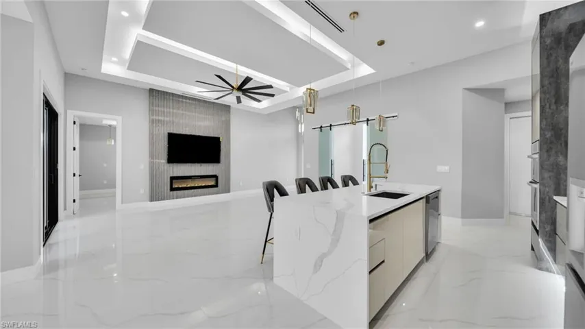 Kitchen featuring modern cabinets, a raised ceiling, a kitchen bar, light stone counters, and light marble finish flooring