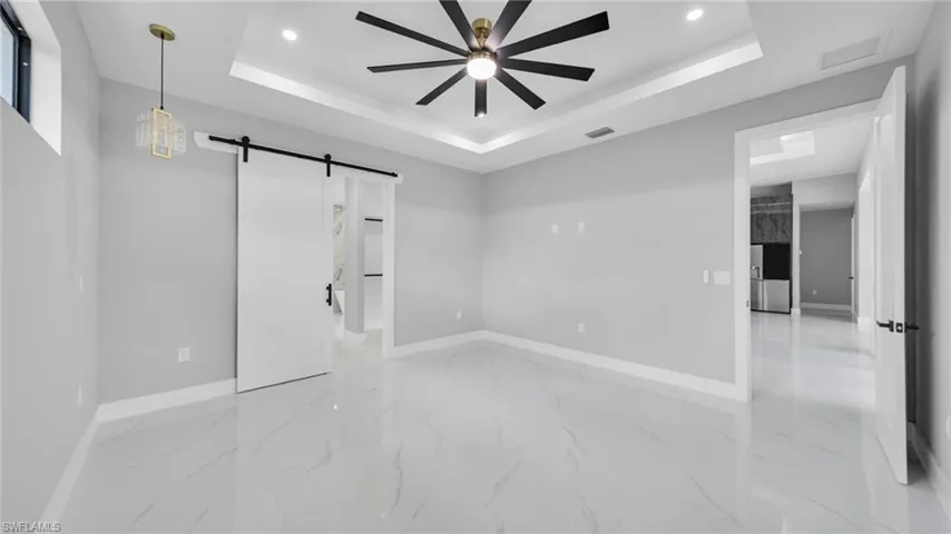 Unfurnished bedroom with a barn door, a raised ceiling, stainless steel fridge, recessed lighting, and a ceiling fan