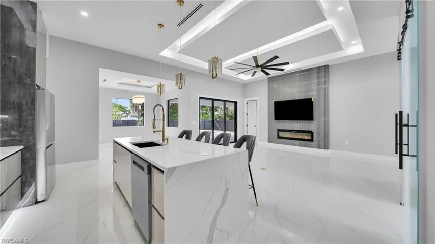 Kitchen with modern cabinets, a tray ceiling, light stone counters, white cabinets, and pendant lighting