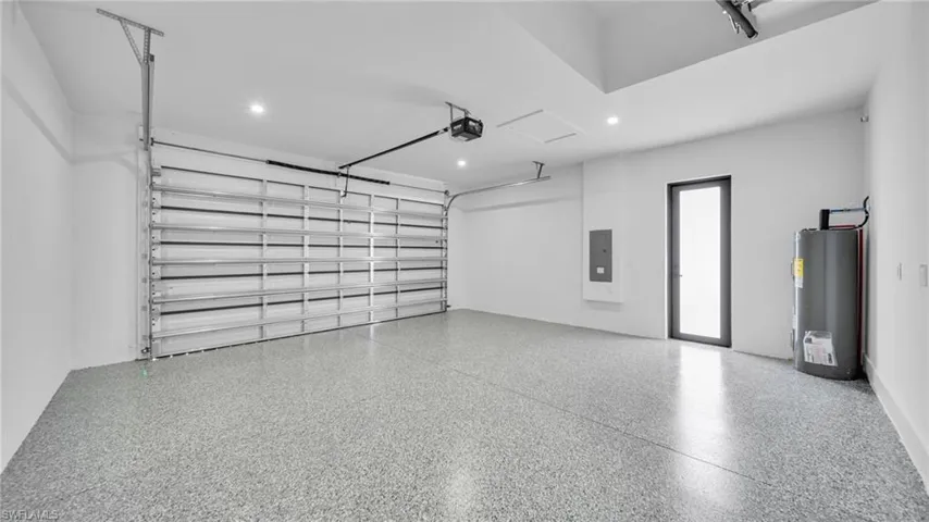 Garage with water heater, electric panel, a garage door opener, and recessed lighting