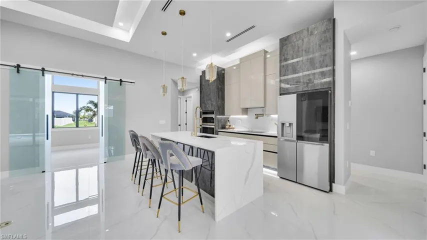 Kitchen with modern cabinets, pendant lighting, stainless steel fridge with ice dispenser, a kitchen island with sink, and light marble finish flooring