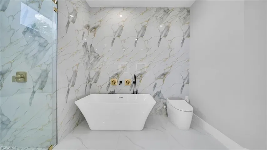 Full bath featuring stone wall, a freestanding tub, marble tiled flooring, and a marble finish shower