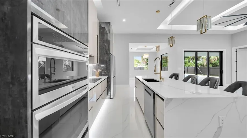 Kitchen featuring modern cabinets, light stone counters, appliances with stainless steel finishes, pendant lighting, and light marble finish floors