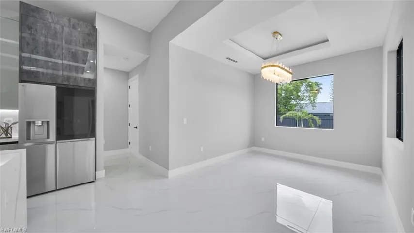 Unfurnished dining area featuring light marble finish floors, a raised ceiling, and a chandelier