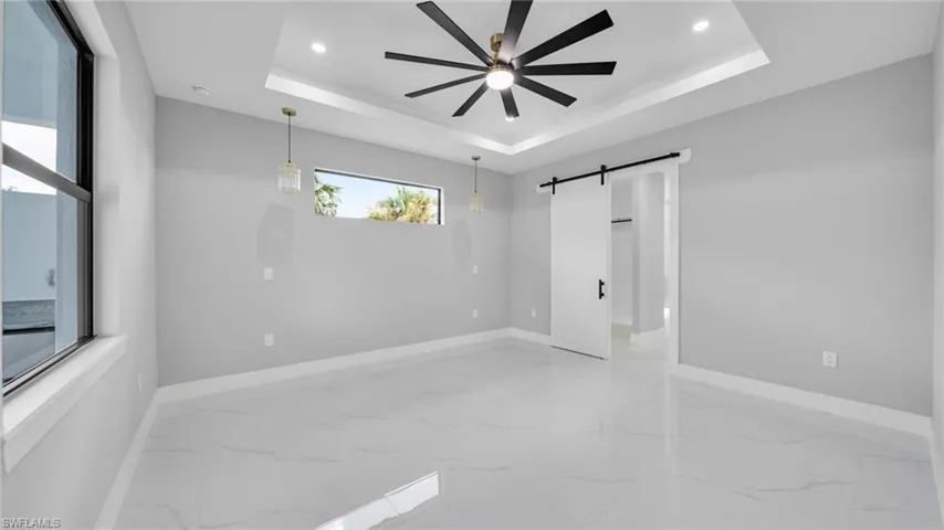 Unfurnished bedroom with light marble finish floors, a tray ceiling, a barn door, ceiling fan, and recessed lighting