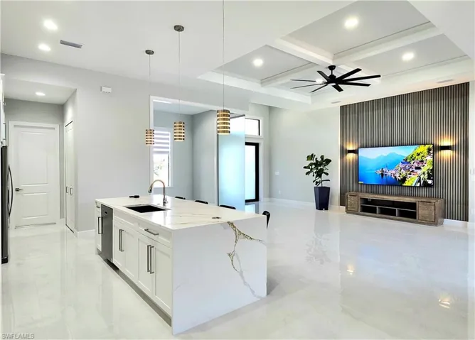 Kitchen with white cabinetry, open floor plan, light stone countertops, a center island with sink, and pendant lighting