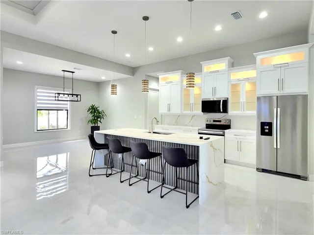 Kitchen with glass insert cabinets, stainless steel appliances, visible vents, white cabinetry, and a center island with sink