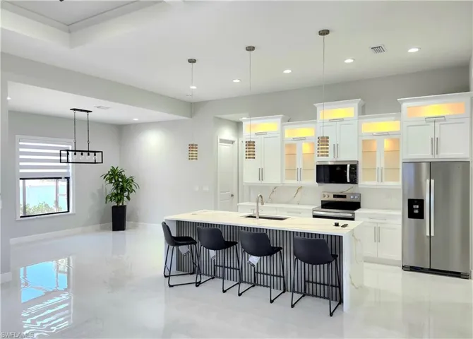 Kitchen with an island with sink, white cabinetry, stainless steel appliances, and light countertops