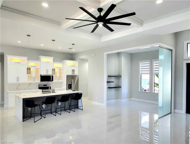 Kitchen featuring a breakfast bar, decorative light fixtures, stainless steel appliances, a large island with sink, and white cabinetry