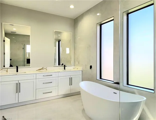 Full bath with double vanity, marble finish floor, a freestanding tub, and a sink