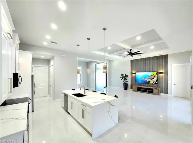 Kitchen featuring a sink, white cabinets, open floor plan, a large island, and decorative light fixtures