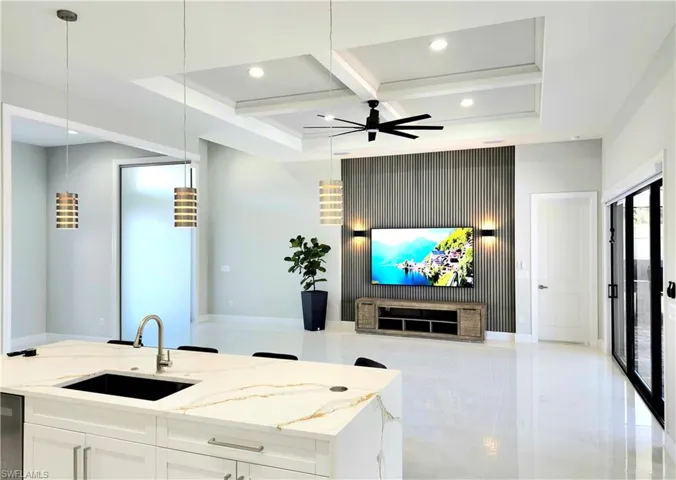 Kitchen featuring a sink, white cabinets, open floor plan, hanging light fixtures, and light stone countertops