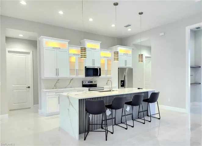 Kitchen featuring stainless steel appliances, white cabinetry, hanging light fixtures, an island with sink, and glass insert cabinets