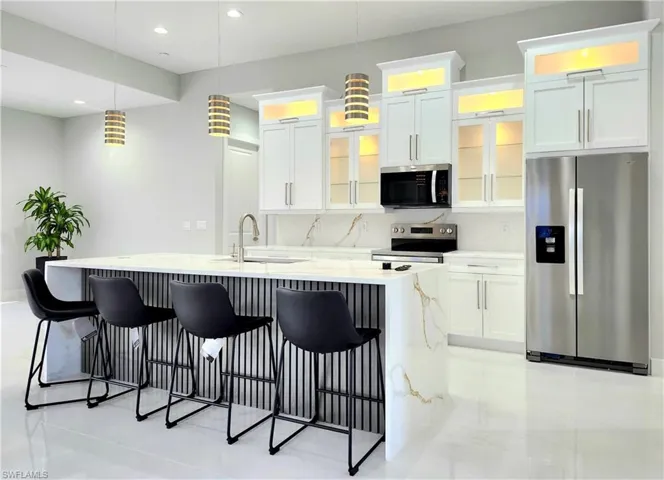 Kitchen with glass insert cabinets, appliances with stainless steel finishes, light countertops, white cabinetry, and a sink