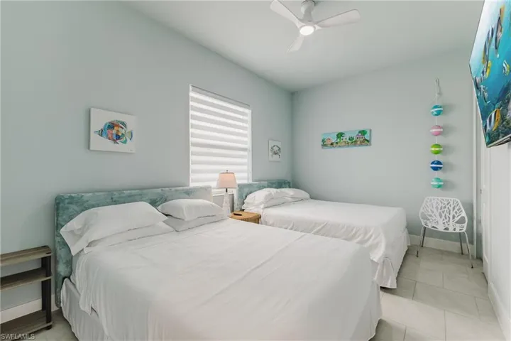 Bedroom featuring two beds with upholstered headboards, a ceiling fan, and tiled flooring