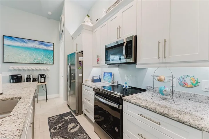 Galley kitchen featuring white shaker cabinetry, speckled countertops, stainless steel appliances, and tile flooring
