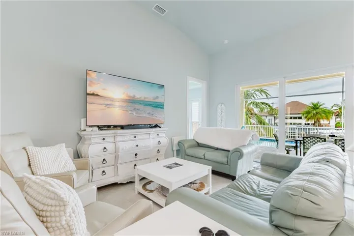 Vaulted ceiling living area featuring light-toned walls, wood-finish flooring, and expansive sliding glass doors opening to the outdoor space