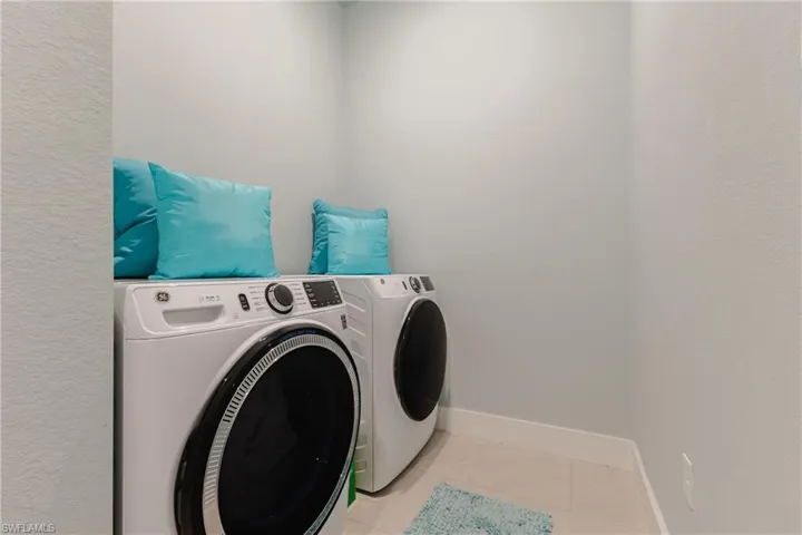 Dedicated laundry alcove featuring neutral wall paint, white baseboards, and tile flooring