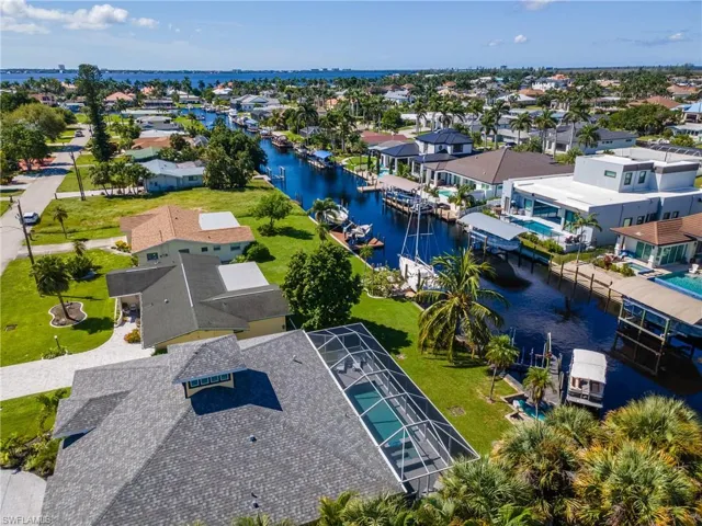 Canal-front property featuring a screened pool enclosure and mature landscaping