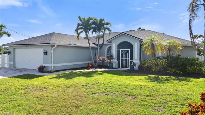 Ranch-style home featuring an attached garage, concrete driveway, a front lawn, roof with shingles, and stucco siding