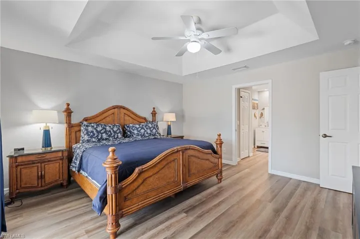 Bedroom featuring a tray ceiling, a ceiling fan, light wood-style flooring, baseboards, and visible vents