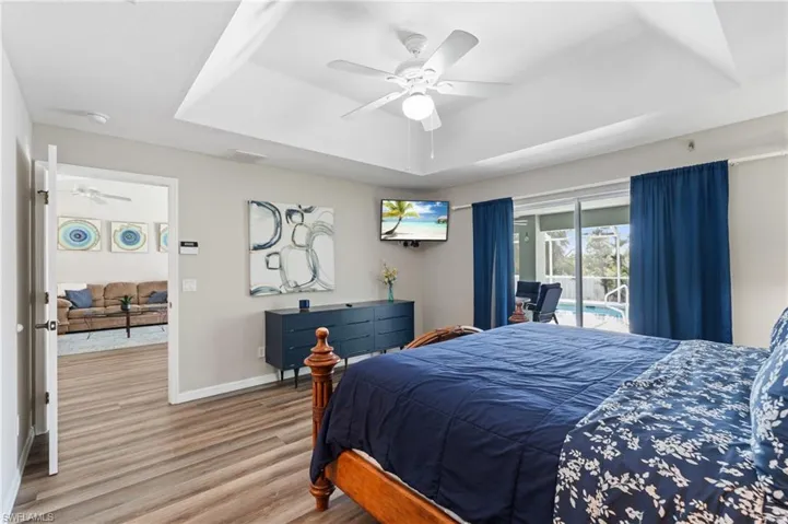 Bedroom featuring a tray ceiling, access to exterior, a ceiling fan, wood finished floors, and baseboards