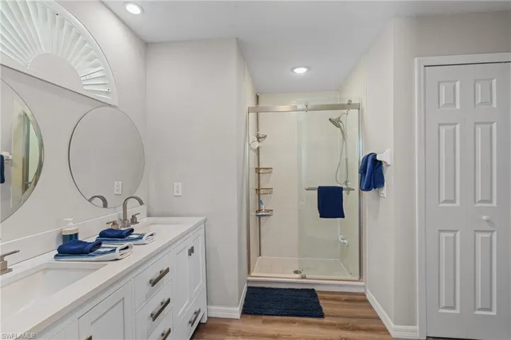 Bathroom with a stall shower, double vanity, wood finished floors, and a sink
